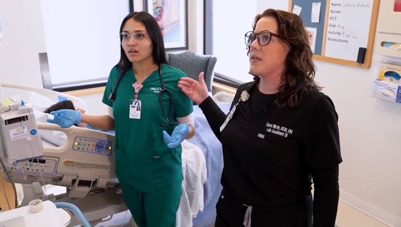 Modal Image Opens to lightbox video - two COD students in the hospital simulation lab looking at a patient's chart