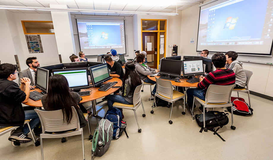 students in a computer class sitting in front of computers while listening to the instructor