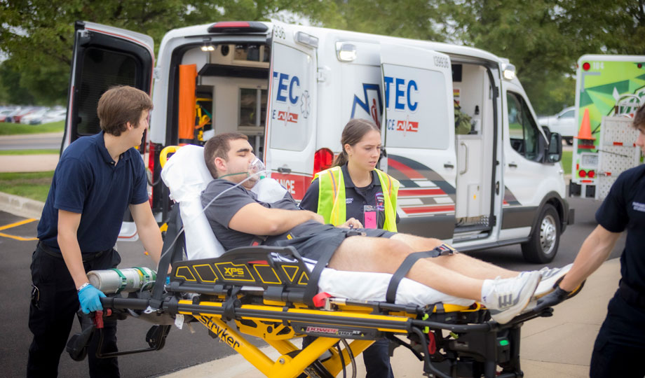 two students wheel a patient wearing an oxygen mask on a stretcher